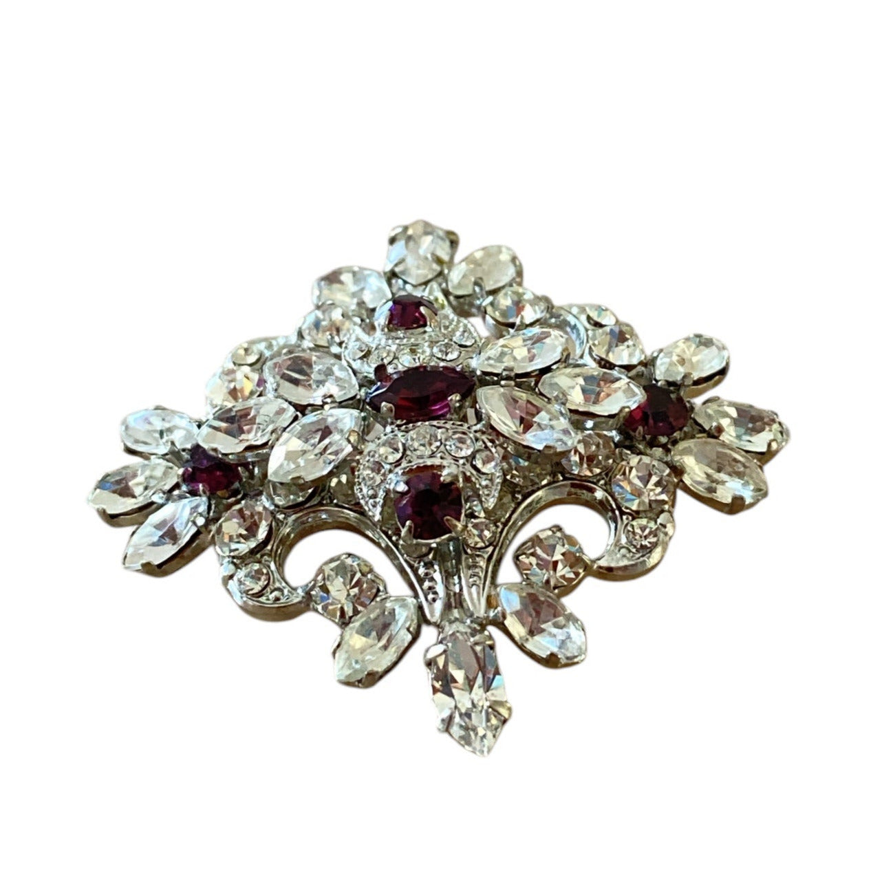 Brosje i sølvfarget metall med fasettslipte lilla og blanke stener