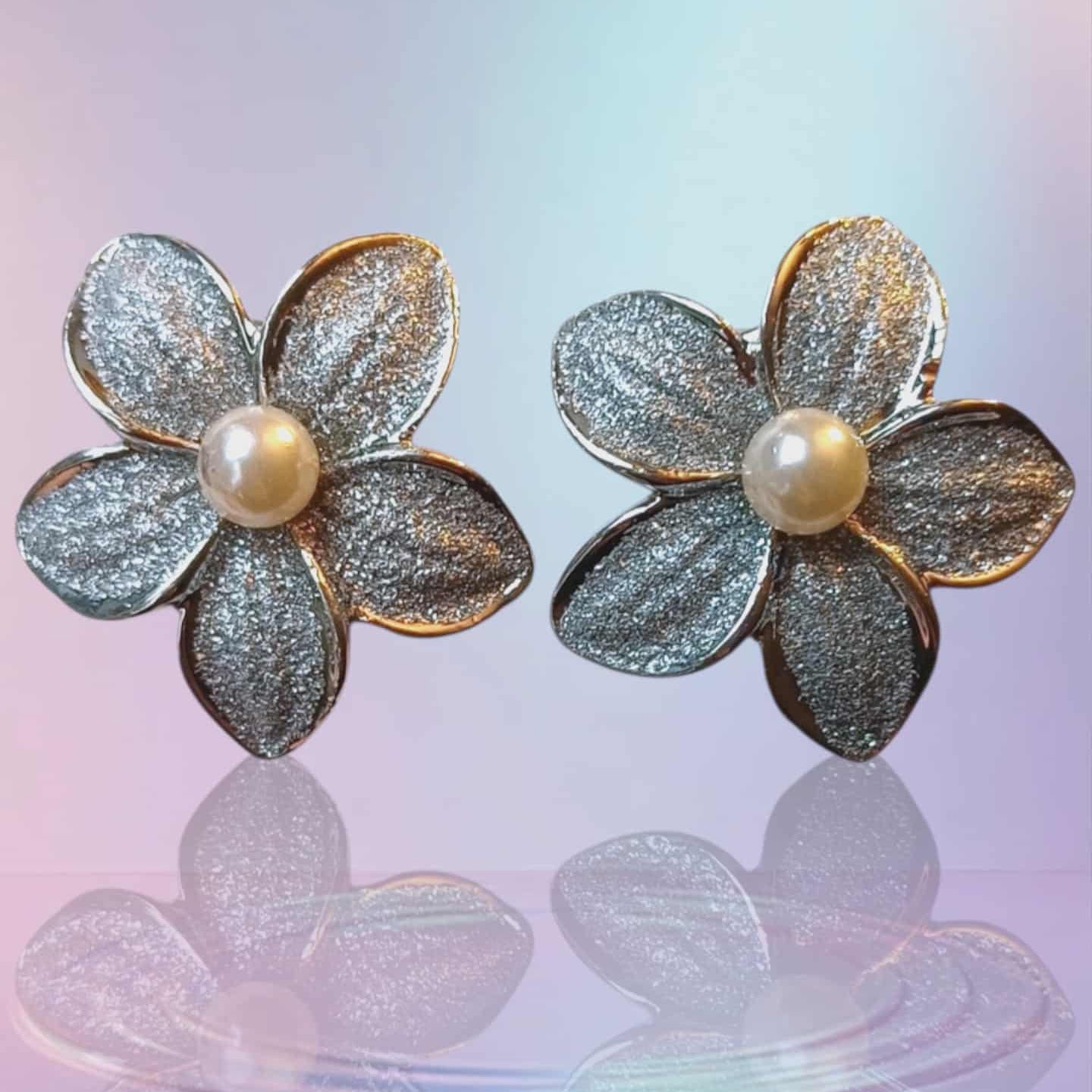 Klipsøredobber i sølvfarget metall med blomst og perledetalj