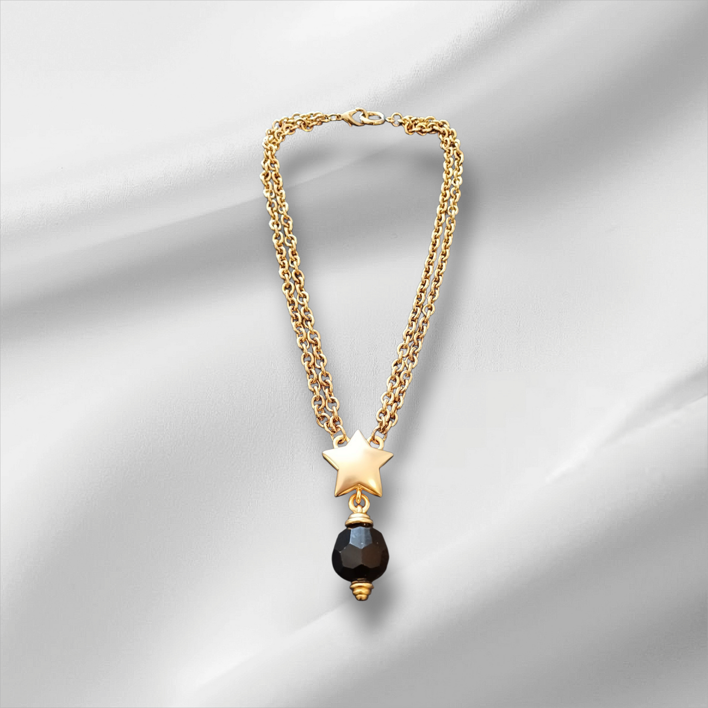 Gullfarget halskjede med stjerneanheng og sort fasettslipt perle