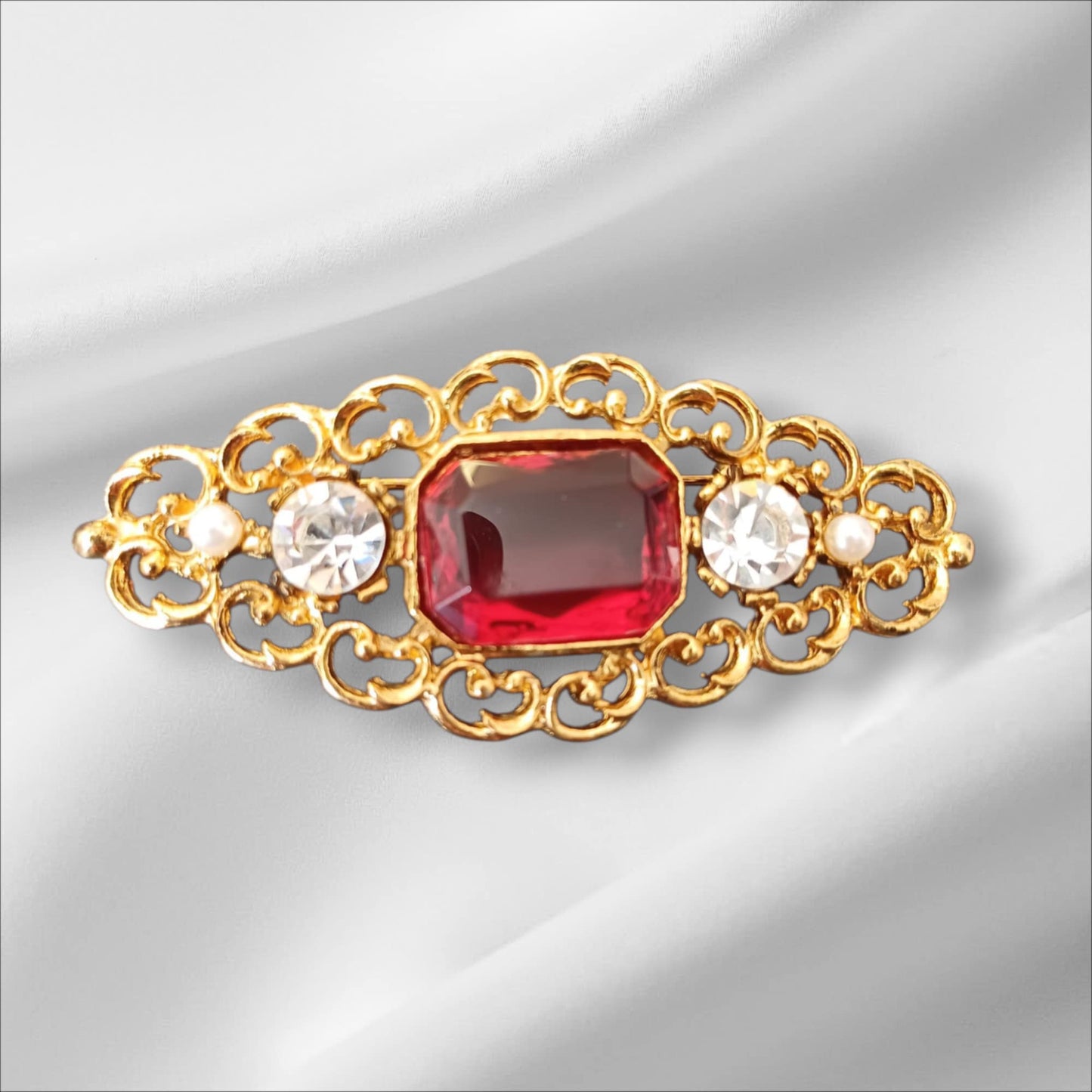 Avlang gullfarget brosje med rød sten og krystaller