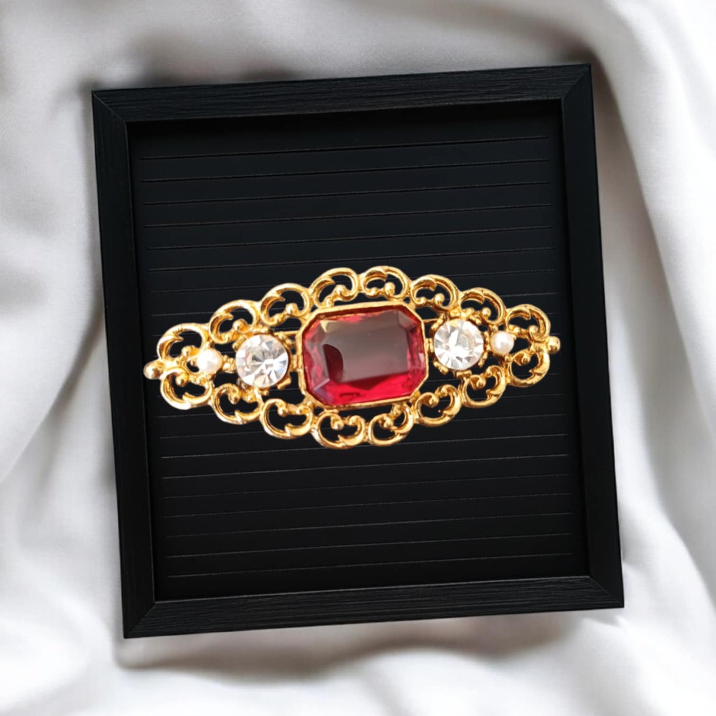 Avlang gullfarget brosje med rød sten og krystaller