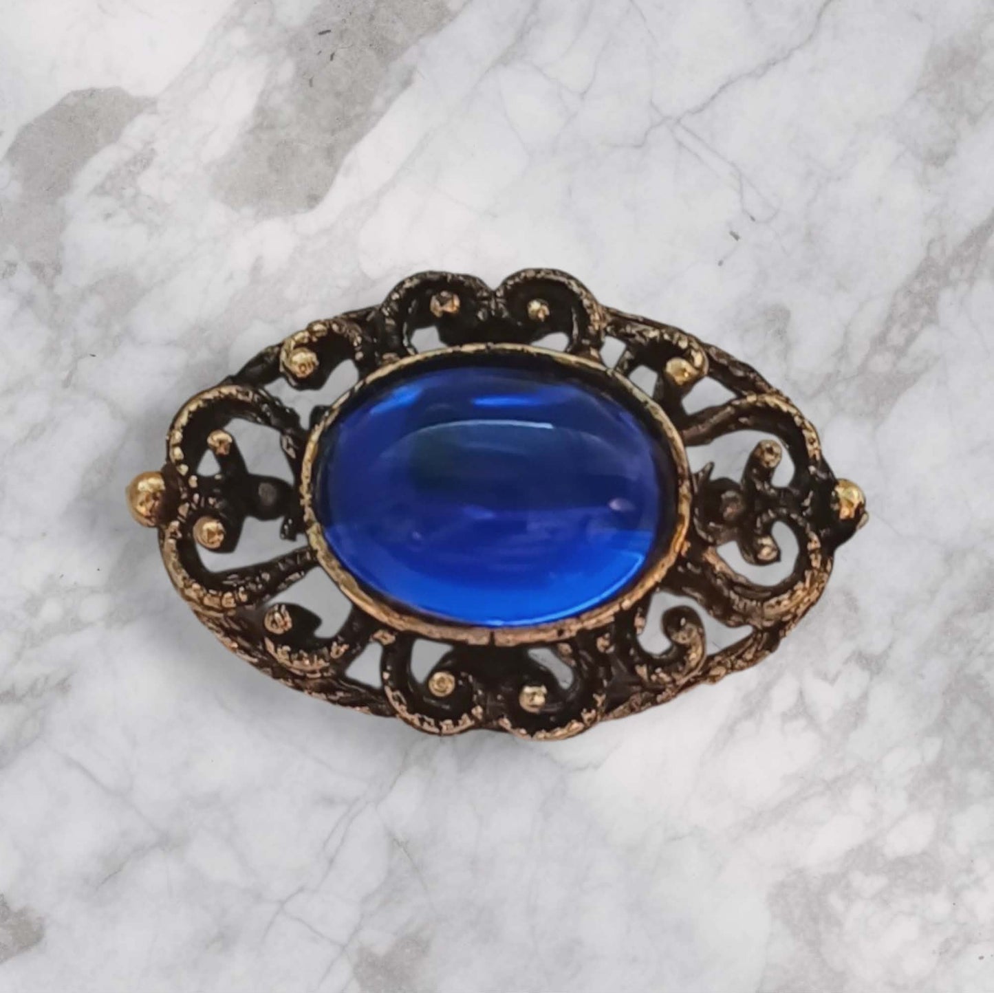 Vintagebrosje med blå sten og ornamentert design