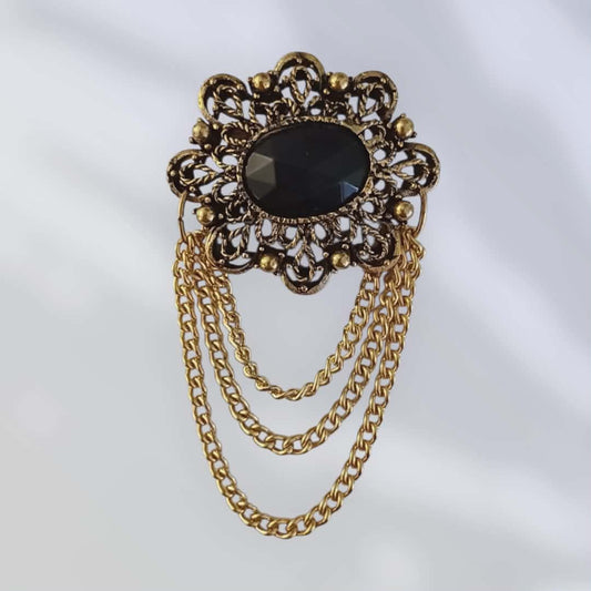 Vintagebrosje med sort sten og dekorative lenker i gullfarget metall