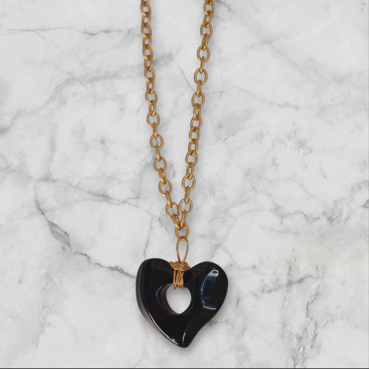 Langt gullfarget halskjede med sort hjerteanheng
